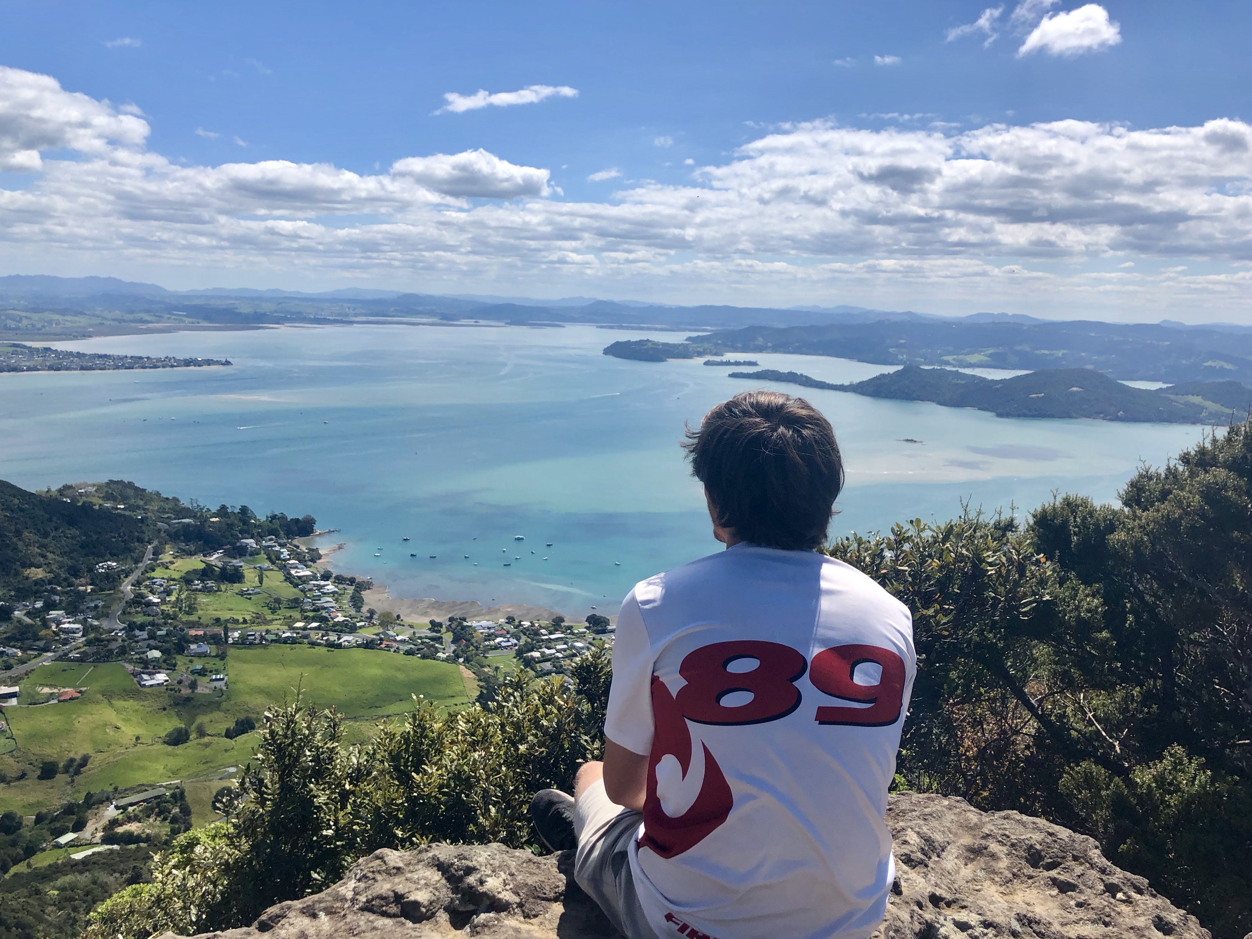 Dan sitting atop Whangerei Heads wearing frisbee kit looking to the sea